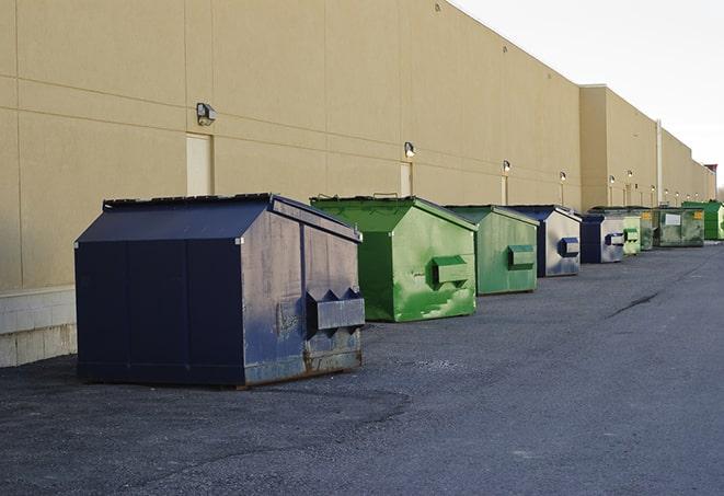 a construction worker unloading debris into a blue dumpster in Bath